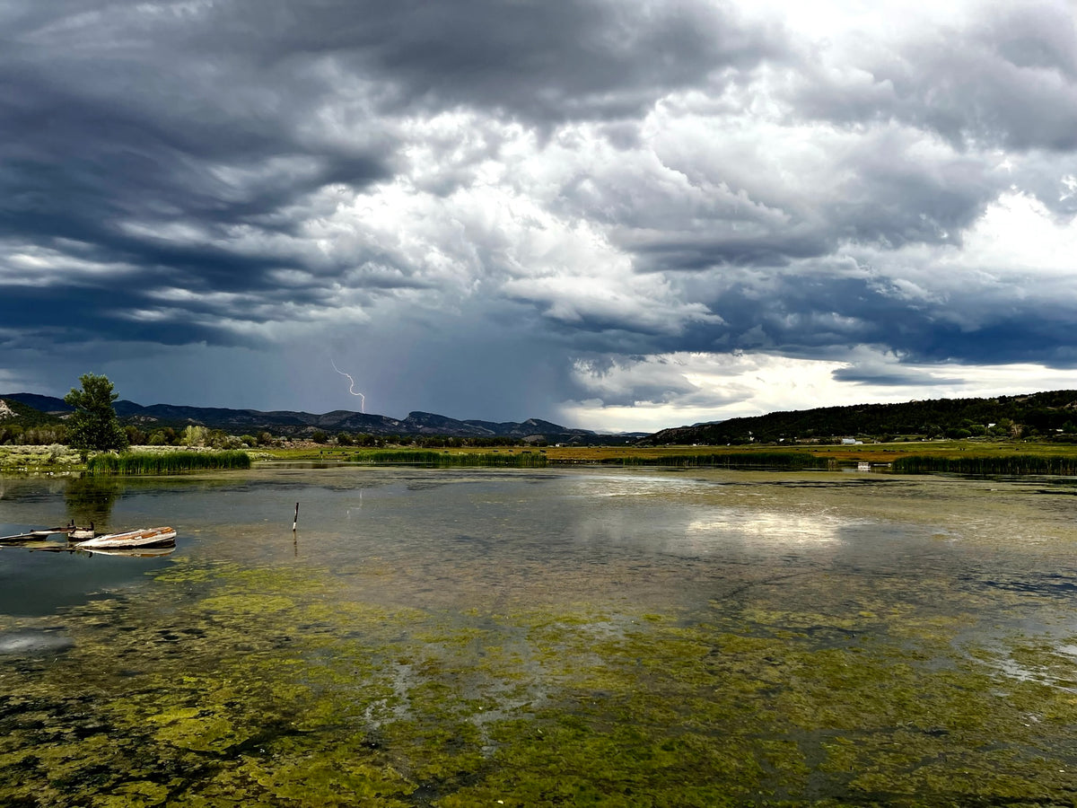 Photo of a pond with lightning striking in the distance in Durango, Colorado by Seth Jennemann